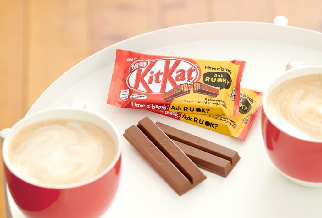 Kit Kat chocolate bars placed between two cups of coffee on a tray, illustrating the brand’s association with coffee breaks