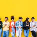 Diverse group of young professionals using smartphones against yellow background, representing how real users engage with platforms like Reddit that AI engines cite for answers instead of brand content.